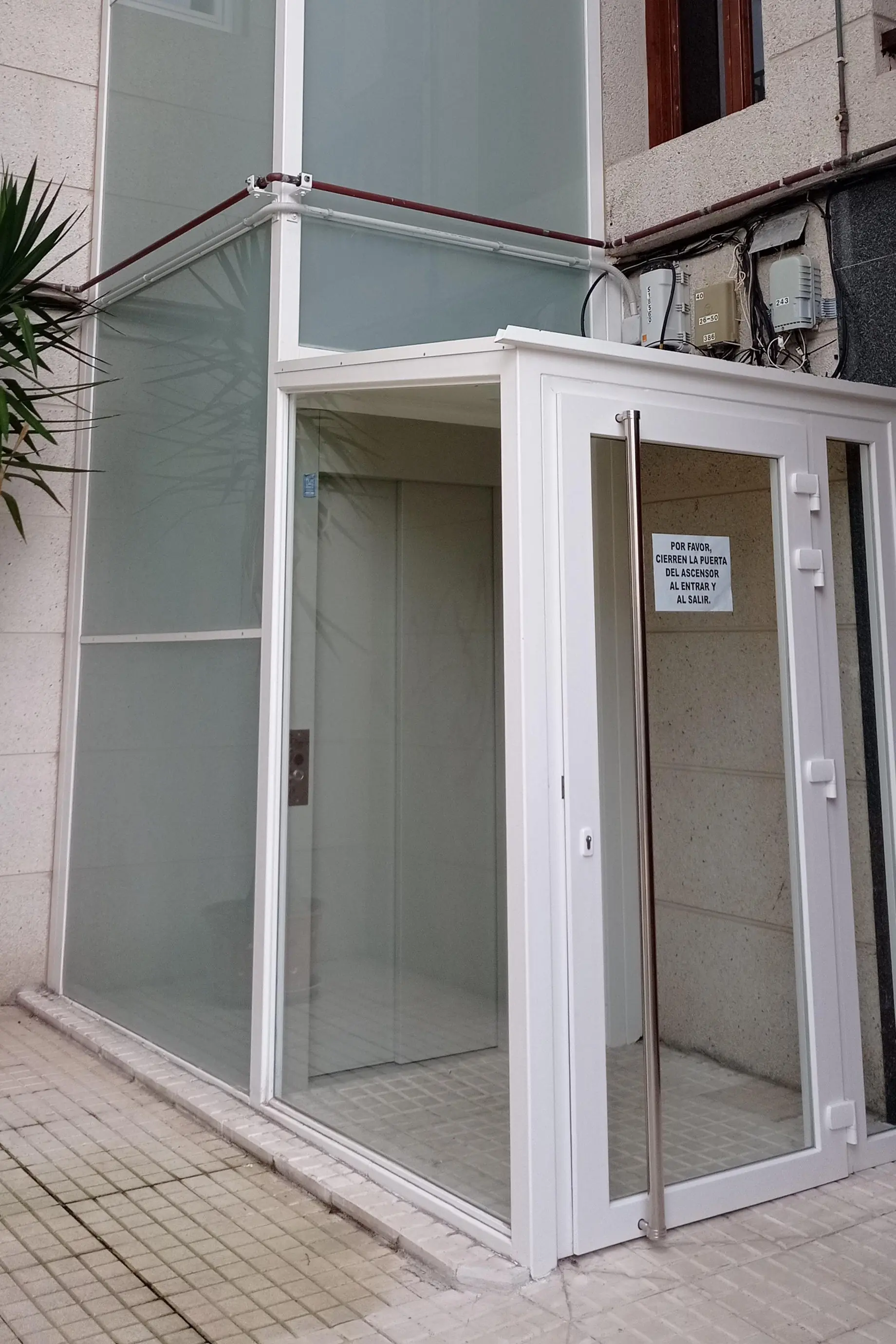Torre acristalada de un ascensor añadido por el exterior de un edificio existente, con el acceso a la cabina al mismo nivel que la acera